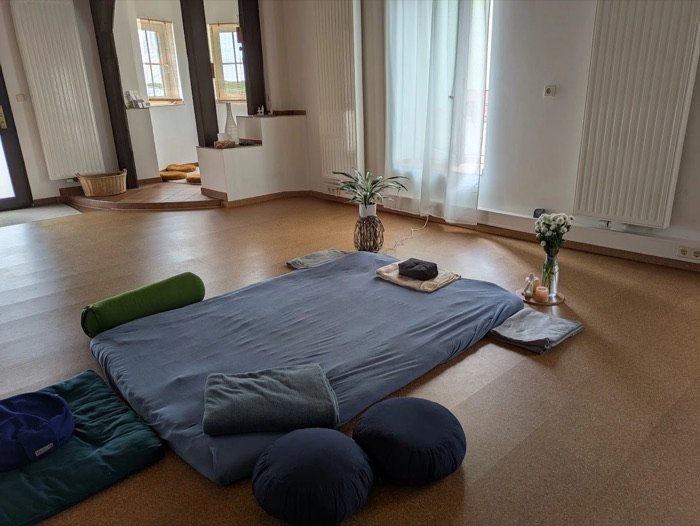 Heller Raum mit großer Matte, Kissen, Bolster, einer Pflanze und frischen Blumen